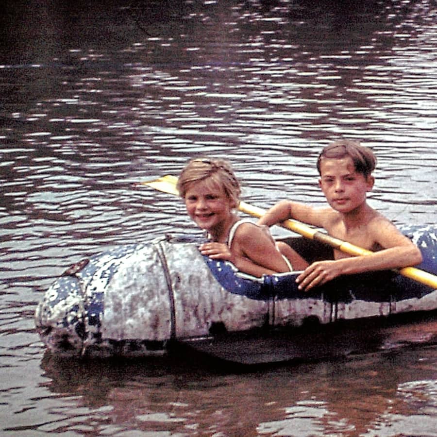 Old photograph of Hartmut as a child, paddling on the water with a girl in an aluminum boat.